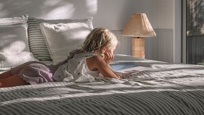 Een slaapkamer met een bed, kussens, een lamp en lijstjes met kunstwerken aan de muur.