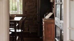 Een smalle keuken met een stenen muur, een koelkast, een eettafel met stoelen en een kast met glazen deuren.