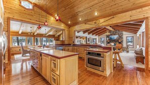 A spacious kitchen with wooden cabinets, a large island, and a stone fireplace. - Bua Northwoods Chalet on the Peninsula (Crystal Falls)