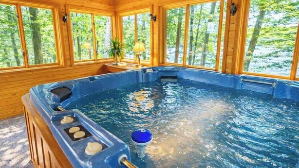 A hot tub in a wooden cabin with large windows and a view of trees. - Bua Northwoods Chalet on the Peninsula (Crystal Falls)