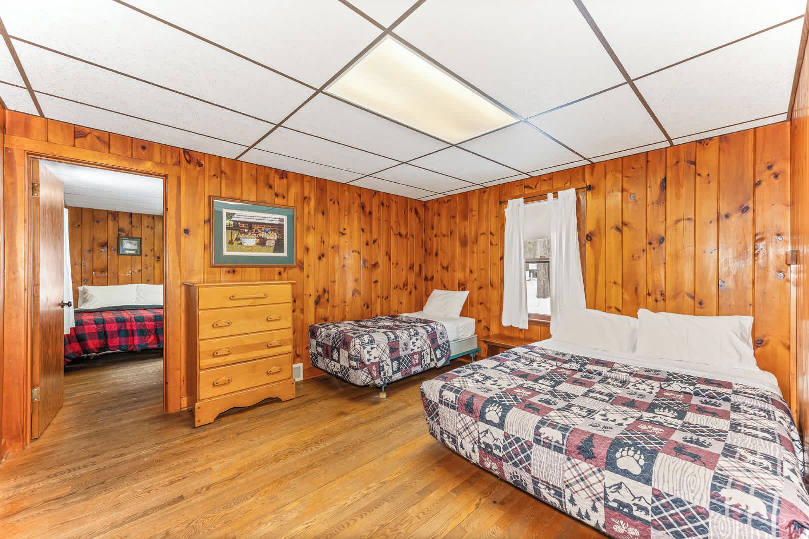 A room with wooden paneling, two beds with patterned quilts, a dresser, and a framed picture on the wall.