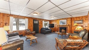 A cozy cabin interior with a fireplace, a television, and a large window overlooking a snowy landscape. - Bayview Cottage 3BR Fireplace Lakefront (Saint Germain)