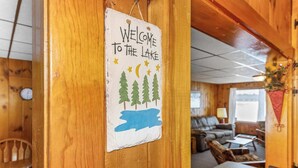 A wooden cabin interior with a welcome sign, a dining area, and a living room with a couch and a coffee table. - Bayview Cottage 3BR Fireplace Lakefront (Saint Germain)