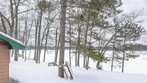A snow-covered landscape with a wooden deck and a building with a green roof. - Bayview Cottage 3BR Fireplace Lakefront (Saint Germain)