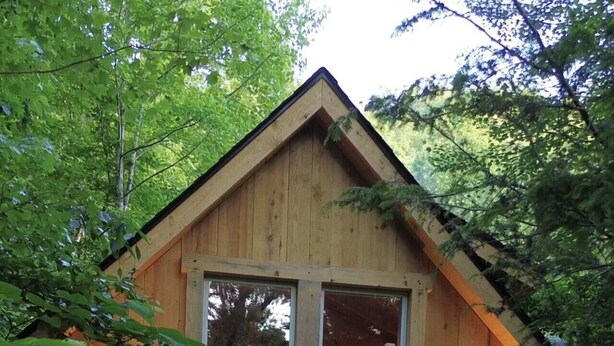 Une cabane en bois dotée d’un balcon, de grandes fenêtres et d’une porte.