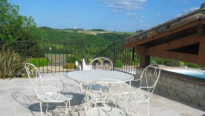 An outdoor patio with a round table and four chairs, surrounded by stone tiles and a metal fence.