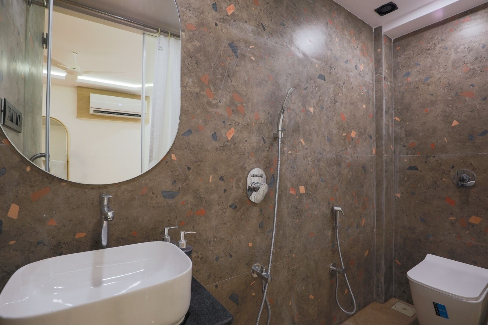 A bathroom with a round mirror, a sink, a shower, and a toilet.