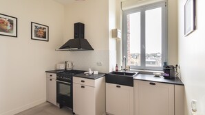 A compact kitchen with a stove, oven, and sink, featuring a window with a city view. - Ker Marlyne - Proche du Port (Dinard)
