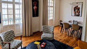 A modern living room with a large window, a dining area with chairs, and a small table. - Ker Marlyne - Proche du Port (Dinard)