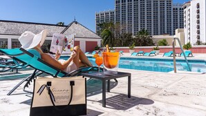 A person relaxing by a pool with lounge chairs, a drink, and a bag labeled "Oceans".