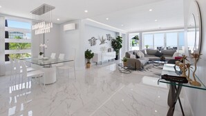 A modern living room with a glass dining table, white chairs, a sofa, and a coffee table.