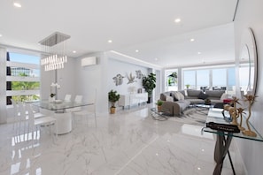 Una sala de estar moderna con una mesa de comedor de vidrio, sillas blancas, un sofá y una mesita de centro.
