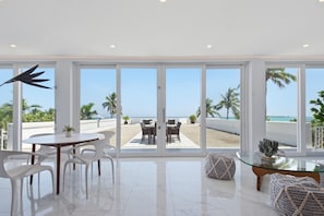Un interior moderno con un gran ventanal que da a una vista de la playa, un comedor con sillas blancas y una mesa de vidrio.
