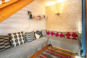 Una habitación acogedora con techo de madera, un sofá con cojines estampados, una estantería y una lámpara fijada a la pared.