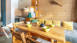 Ein gemütlicher Essbereich mit Holztisch und -stühlen, im Hintergrund eine Küche und eine Holzwand mit einem dekorativen Gegenstand.