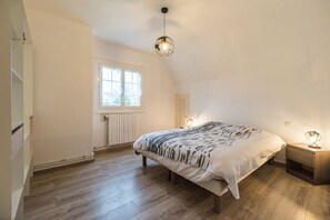 Ein Schlafzimmer mit einem großen Bett, einem Fenster, einem Heizkörper und einem Nachttisch mit einer Lampe.