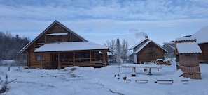 Eine Holzhütte mit schneebedecktem Dach, Schornstein und einer Holzterrasse.