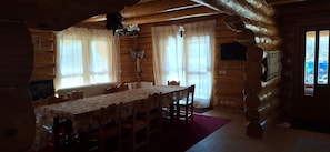 Ein Holzblockhaus-Interieur mit Esstisch, Stühlen, einer Chandelüster und einem Fernseher.