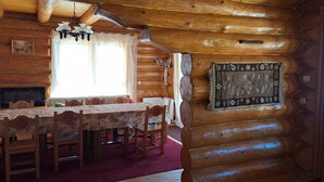 L’intérieur d’une cabane en rondins, avec une table à manger, des chaises, une cheminée, un lustre et un tapis à motifs.