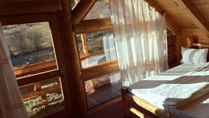 Une chambre dans une cabane en bois, avec un lit, des rideaux et une vue sur l’extérieur.