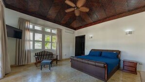 A bedroom with a large bed, a ceiling fan, a TV mounted on the wall, and a window with curtains. - Villa Zaphira (Puerto Plata)