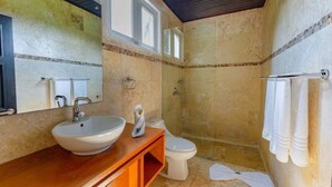 A bathroom with a wooden vanity, a white sink, a toilet, and a shower area. - Villa Zaphira (Puerto Plata)