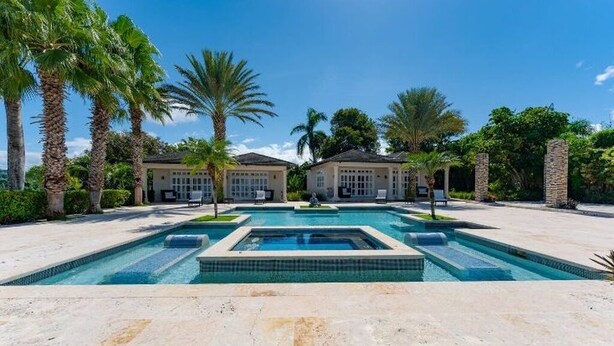 A pool area with two buildings, palm trees, and a clear sky. - Villa Zaphira (Puerto Plata)
