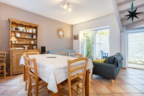 Een eetgedeelte met een tafel en stoelen, een houten kast met keukengerei, een bank en een groot raam met uitzicht.