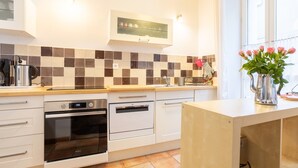 Una cocina moderna con armarios blancos, un salpicadero de azulejos y una encimera con un hervidor y un jarrón de flores.