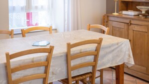 Un comedor con una mesa cubierta por un mantel blanco, sillas de madera, una lámpara sobre la mesa y una ventana con cortinas.