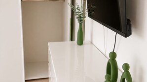Une console blanche sur laquelle sont posés un téléviseur à écran plat, un vase vert et des sculptures abstraites.