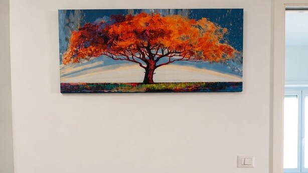 Une chambre à coucher avec un lit, des oreillers, un tableau représentant un arbre et une vue sur une fenêtre.