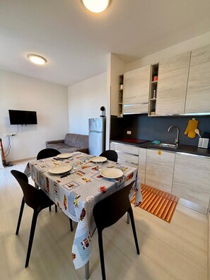 A modern kitchen with built-in cabinets, a dining table set for four, a flat-screen TV mounted on the wall, and a refrigerator. - The Blue Knoll apartment (Cavaion Veronese)