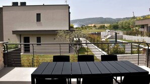 Un balcone con tavolo e sedie, affaccia su una zona residenziale con case e cielo sereno.