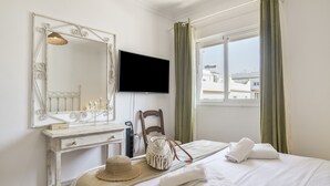 Ein Hotelzimmer mit Bett, Schminktisch mit Spiegel, Fernseher und einem Fenster mit Vorhängen.