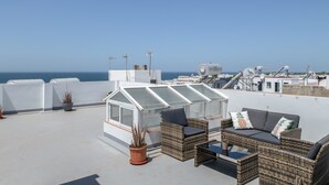 Eine Dachterrasse mit Korbmöbeln, einem Glashaus und Blick auf das Meer.