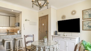 Ein Essbereich mit rundem Tisch, Barhocker, einem Fernseher und einer Küche im Hintergrund.