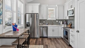 A modern kitchen with white cabinets, stainless steel appliances, a built-in oven, and a window with blinds. - The CODtage is amazing! 60 steps from beach, 2.5 blks to boardwalk! (Carolina Beach)