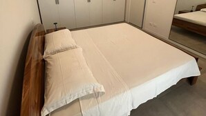 Ett sovrum med en stor säng, en sänggavel i trä, ett vitt garderobsskap och en luftkonditioneringsenhet på väggen.