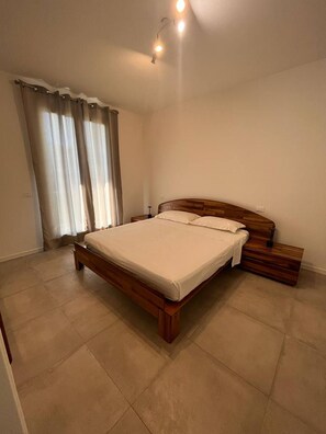 A bedroom with a wooden bed, a nightstand, a lamp, and a window with curtains. - Villetta Sabri - Vacation Home in Garda (Garda)