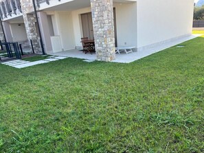 A modern building with a stone pillar, a covered patio with a table and chairs, and a well-maintained lawn. - Villetta Sabri - Vacation Home in Garda (Garda)
