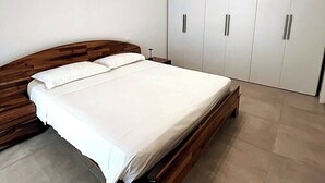 A bedroom with a wooden bed, white bedding, and a wardrobe with silver handles. - Villetta Pima - Holiday Home in Garda (Garda)