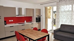 A modern kitchen with a wooden table and red chairs, a grey sofa, and a sliding glass door to a garden. - Villetta Pima - Holiday Home in Garda (Garda)