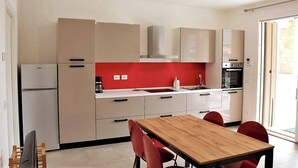 A modern kitchen with white cabinets, a red backsplash, and a wooden dining table with red chairs. - Villetta Pima - Holiday Home in Garda (Garda)