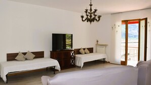 A hotel room with two single beds, a TV on a wooden cabinet, a chandelier, and a balcony with a view. - Villa Tessari in Rivoli Veronese (Rivoli Veronese)