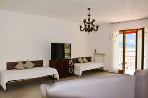 Ein Hotelzimmer mit zwei Einzelbetten, einem Fernseher auf einer Holzkommode, einer Kandelaber und einem Balkon mit Blick.