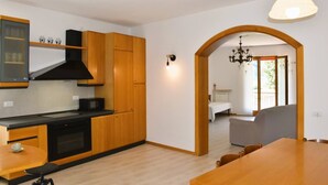 A modern kitchen with wooden cabinets, a black microwave, and a dining area with a wooden table and chairs. - Villa Tessari in Rivoli Veronese (Rivoli Veronese)