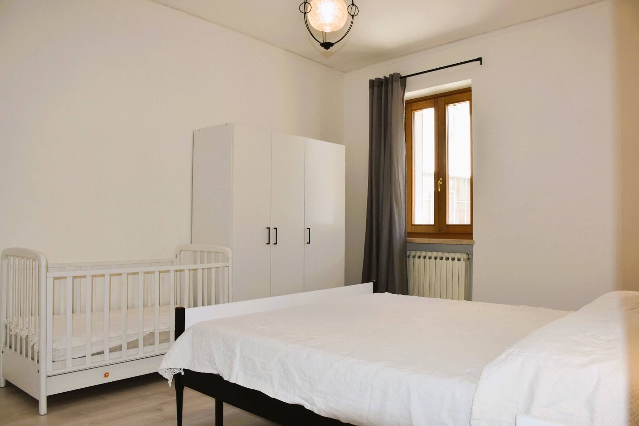 Ein Schlafzimmer mit einem Kinderbett, einem Bett, einem Kleiderschrank und einem Fenster mit Vorhängen.