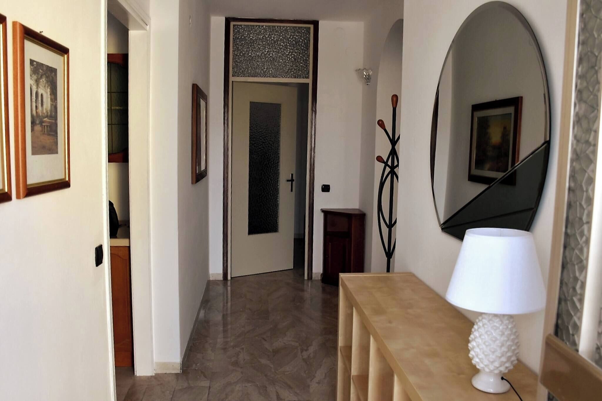 A hallway with a wooden bench, a white lamp, a mirror, and framed pictures on the wall.