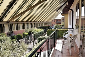 Ein Balkon mit gestreiftem Markisenvorzelt, einem kleinen Tisch mit Stühlen und Blick auf ein Wohngebiet mit Häusern und Grünflächen.